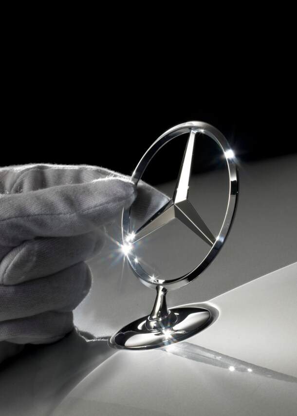 Eine Hand fasst einen Mercedes-Stern an.