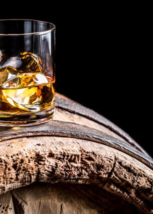 Ein Glas Whiskey mit Eiswürfeln auf einem alten hölzernen Barrel