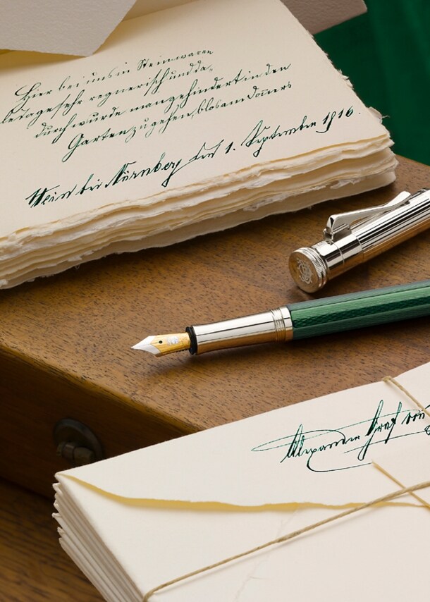 Ein grün-silberner Füllfederhalter auf hölzernem Untergrun zwischen zwei nostalgischen Briefstapeln