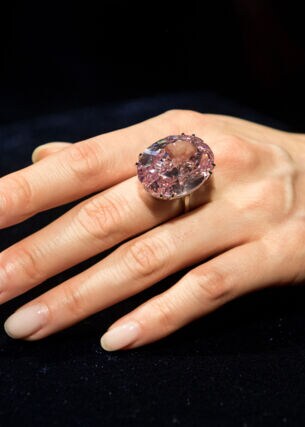 Eine weibliche Hand mit einem großen, rosafarbenen Diamantring am Mittelfinger