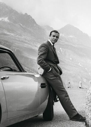 Sean Connery alias James Bond lehnt an einem Aston Martin DB5.