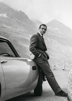 Sean Connery alias James Bond lehnt an einem Aston Martin DB5.