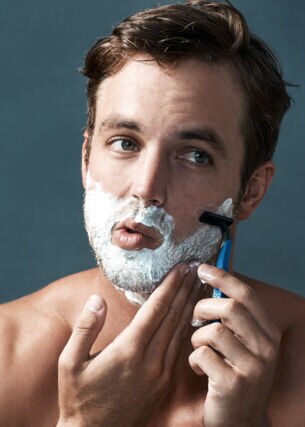 Ein Mann hat Rasierschaum im Gesicht und rasiert sich.
