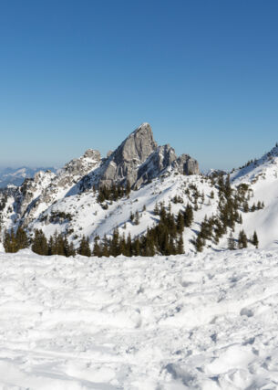 Blick auf die teilweise verschneiten Gipfel des Mangfallgebirges bei blauem Himmel