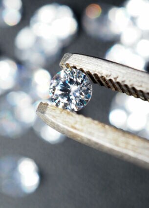 Ein runder Diamant wird von einer Pinzette gehalten