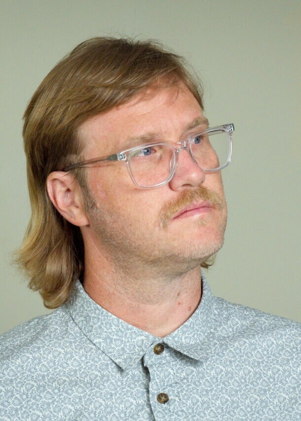 Ein Mann mit einem Mullet-Haarschnitt und Brille