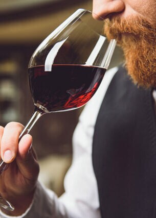 Ein Mann mit Bart riecht an einem Rotweinglas