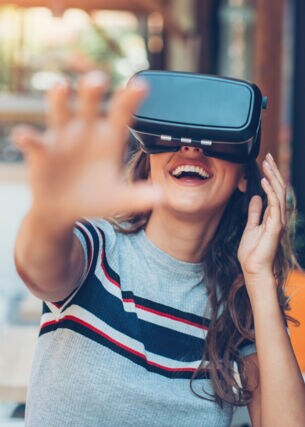 Eine Frau mit VR-Brille lacht und greift in die Luft