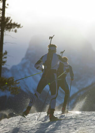 Drei Männer auf Skiern mit einem Biathlon-Gewehr auf dem Rücken fahren durch den Schnee.