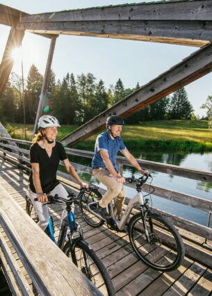 Ein Paar auf Fahrrädern fährt über eine Holzbrücke über einen Fluss