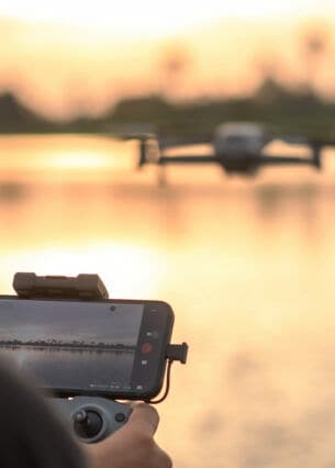 Rückansicht einer Person, die mit einer Drohne per Smartphone einen See fotografiert.