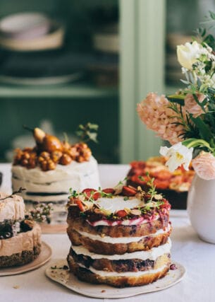 Fünf hausgemachte, stilvoll dekorierte Torten stehen auf einem Küchentisch neben einem Blumenstrauß