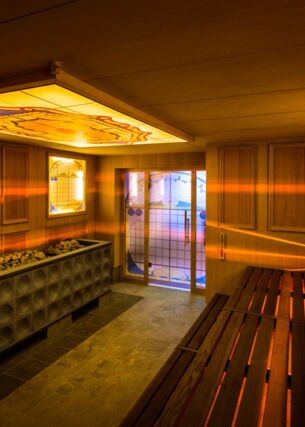 Holzsauna mit gelben, dekorierten Glasplatten, durch die Lichtstrahlen ins Innere dringen