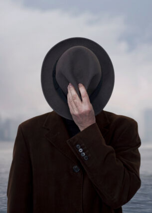 Ein Schwarz-Weiß-Bild einer Person, die sich einen Hut vor das Gesicht hält