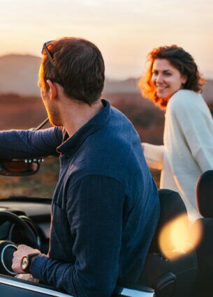 Rückansicht eines Paares auf Reise, das aus einem Cabriolet in eine Wüstenlandschaft bei Sonnenuntergang schaut