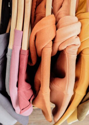 Eine Reihe Sweatshirts in bunten Pastellfarben auf Kleiderbügeln aus Holz