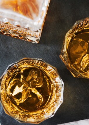 Aufsicht von zwei gefüllten Whiskygläsern mit Eis auf einer Schieferplatte