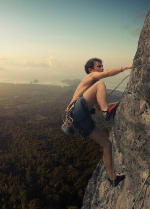 Ein junger Mann klettert an einer Felswand, während die Sonne untergeht