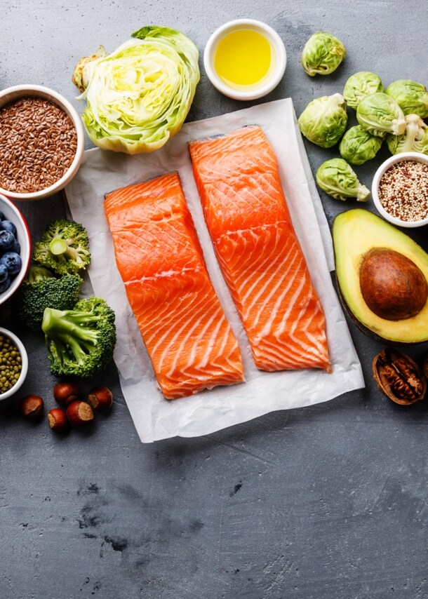 Gesunde Lebensmittel wie Lachs, Avocado, Granatapfel und mehr nebeneinander.