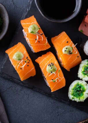 Veganes Sushi auf einer Schieferplatte angerichtet mit Sojasauce und Algensalat