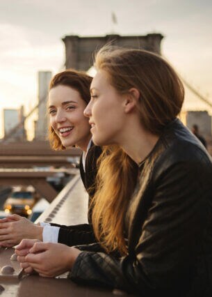 Zwei junge Mädchen stehen lächelnd auf der Brooklyn Bridge vor der Skyline Manhattans