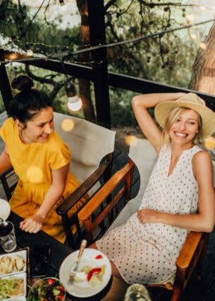 Zwei Frauen sitzen gut gelaunt beim sommerlichen Outdoor-Dinner an einem Tisch auf einer Holzterrasse