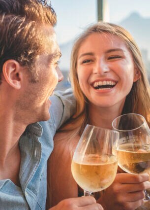 Ein Paar sitzt lachend nebeneinander und stößt mit Weingläsern an