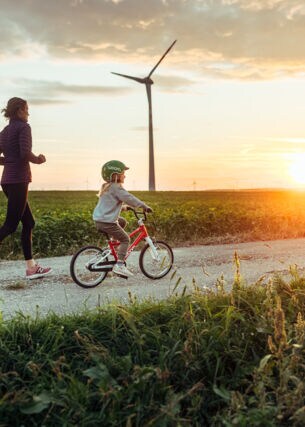 Eine joggende Frau ist mit einem kleinen Mädchen auf dem Fahrrad bei Sonnenuntergang unterwegs