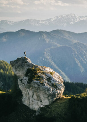 Eine Person beim Wandern auf einem Felsen umgeben von Bergen