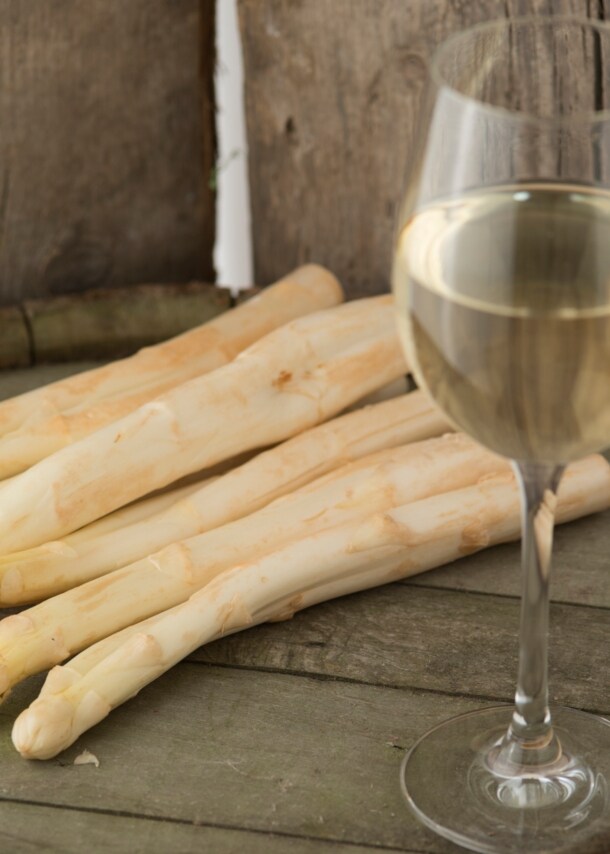 Ein Glas Wein und mehrere Stangen Spargel auf einem Fass Wein