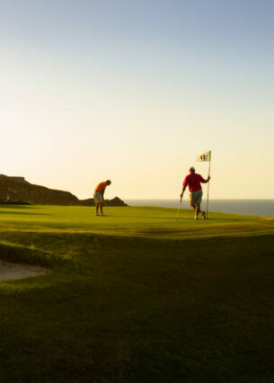 Zwei Golfspieler beim Abschlag auf einer Golfanlage im Sonnenuntergang