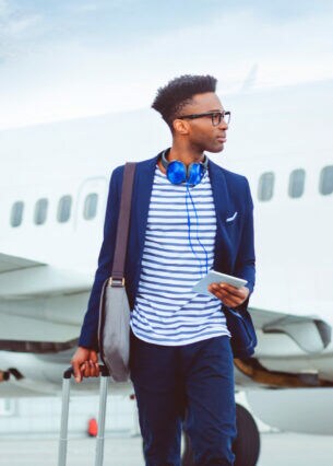 Ein junger, stylisher Geschäftsmann mit Reisegepäck vor einem Flugzeug