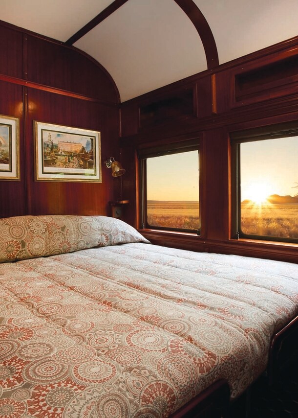 Der Innenraum eines Luxuszugs mit Doppelbett und Blick nach draußen in die Natur.