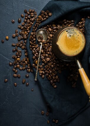 Geröstete Bohnen und frisch gebrühter Kaffee auf einem dunklen Tuch angerichtet