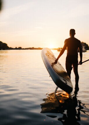 Mann trägt ein SUP Board ins Wasser