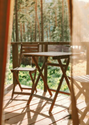 Blick auf eine Holzterrasse mit Stühlen und Tisch, im Hintergrund Wald