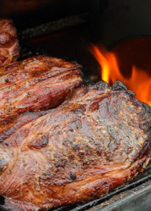 Fleisch wird indirekt neben einer Flamme im Grill gegrillt