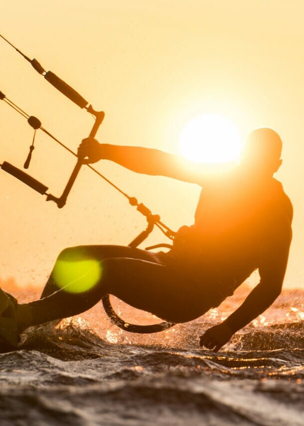 Silhouette des Kitesurfers, der bei schönem Sonnenuntergang mit Sonne neben dem Fahrerkopf reitet