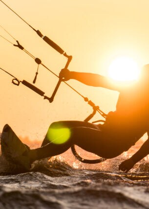 Silhouette des Kitesurfers, der bei schönem Sonnenuntergang mit Sonne neben dem Fahrerkopf reitet