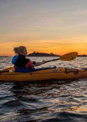 Eine Frau in einem Kajak auf einem Gewässer bei Sonnenuntergang