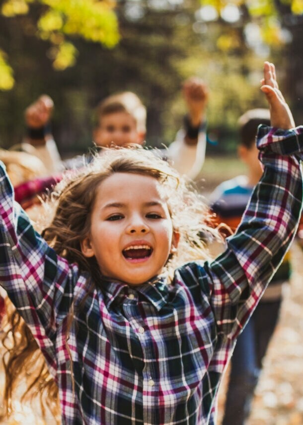 Vier fröhliche Kinder rennen im Freien durchs Laub