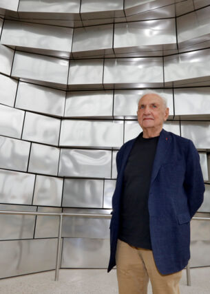 Architekt Frank Gehry vor einer Fassade aus glänzenden Aluminiumplatten