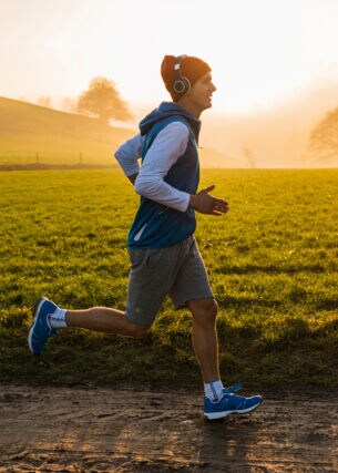 Ein junger Mann joggt im Morgengrauen an einer Wiese entlang