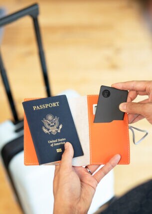 Eine Person hält einen Reisepass und einen Schlüsselfinder in der Hand