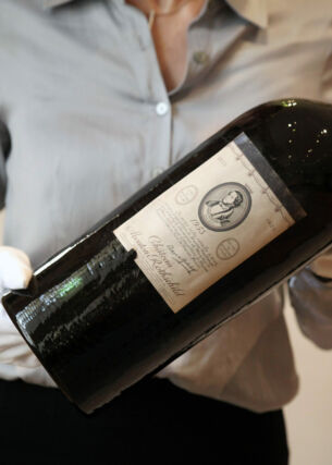 Eine große Flasche Rotwein der Marke Chateau Mouton Rothschild wir von einer Person mit weißen Handschuhen gehalten