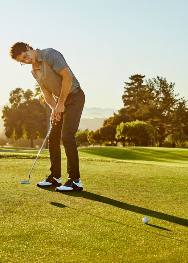 Ein Mann steht auf einem Golfplatzt und locht gerade den Golfball ein.