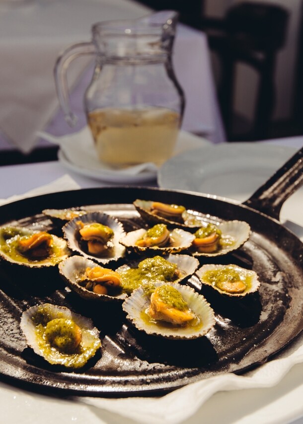 Napfschnecken mit grüner Soße, angerichtet auf einer Grillpfanne auf einem Restauranttisch