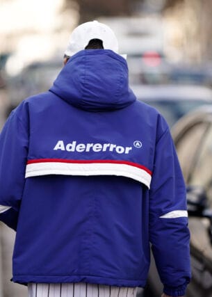 Rückansicht eines Mannes auf einer Straße mit blauer Trainingsjacke mit dem Markennamen Adererror