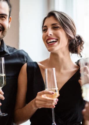 Ein fröhliches Paar in festlichen Outfits mit einem Glas Champagner in den Händen.