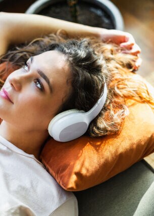 Eine Frau mit Kopfhörern liegt entspannt auf einem Sofa